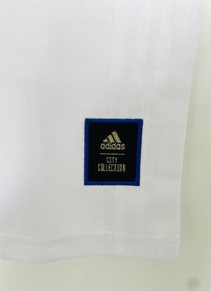 Camiseta blanca Adidas estilo retro con hombros rojos y azules y flor de lis dorada, supuestamente conmemorativa de París 2020. — foto 2