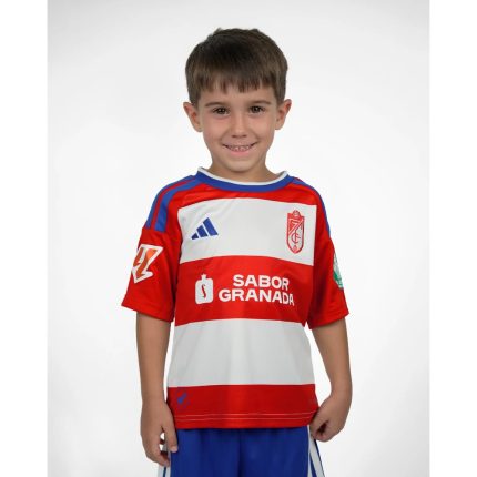 Primera equipación oficial del Granada CF para niños, temporada 2026-27. Conjunto de camiseta y pantalón rojiblancos.