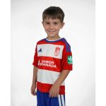 Primera equipación oficial del Granada CF para niños, temporada 2026-27. Conjunto de camiseta y pantalón rojiblancos.