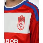 Primera equipación oficial del Granada CF para niños, temporada 2026-27. Conjunto de camiseta y pantalón rojiblancos.